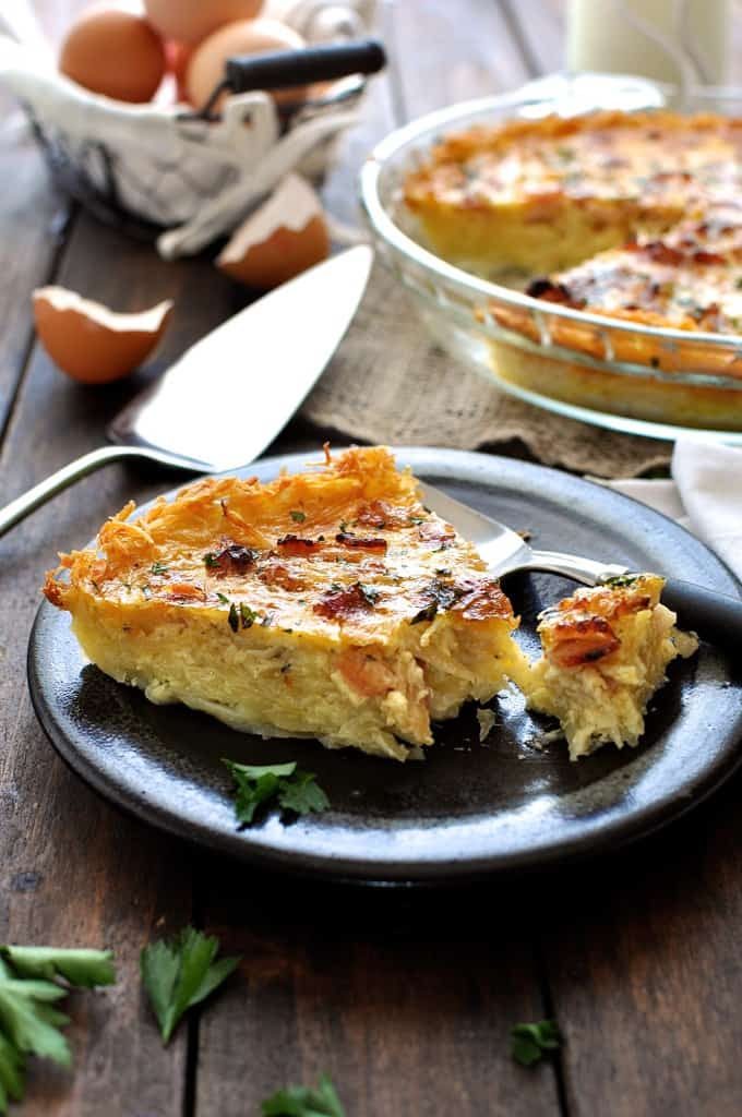 Slice of Hash Brown Crust Quiche Lorraine on a dark brown plate, ready to be eaten.