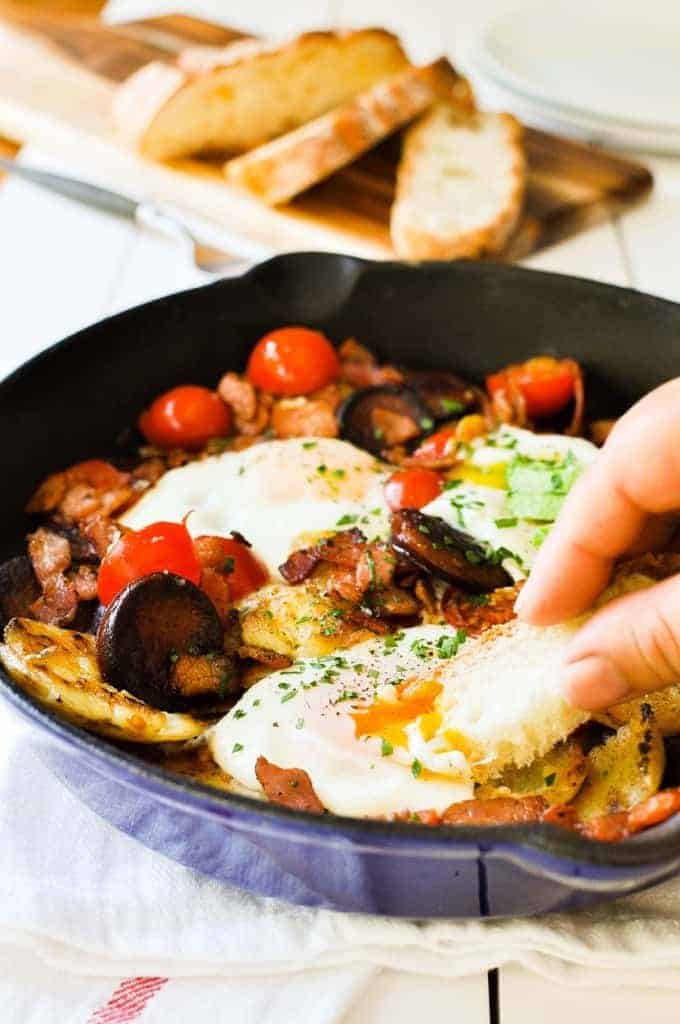Dipping bread into the egg yolk on a Chorizo Breakfast Hash with Bacon and Smashed Potatoes