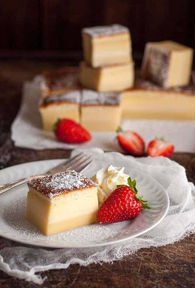 A slice of Magic Three Layer Custard Cake on white plate with strawberries