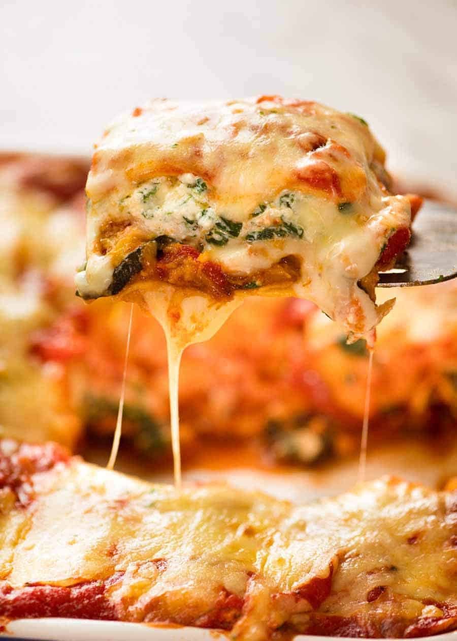 A piece of Vegetarian Lasagna being scooped out of a casserole dish, fresh out of the oven.