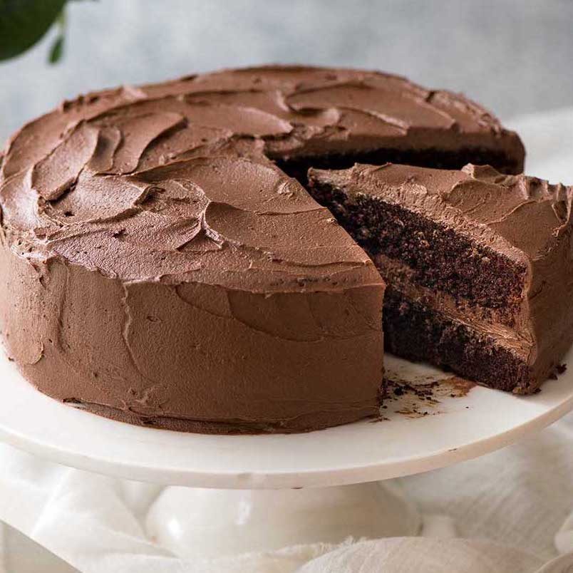 Chocolate Cake with buttercream frosting on a white cake stand, ready to be cut and served