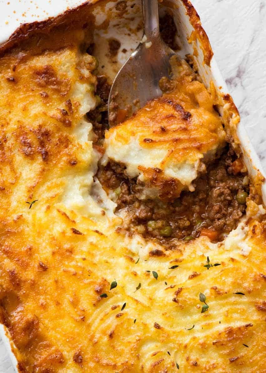 Overhead photo of spoon scooping Shepherd's Pie out of baking dish, fresh out of the oven.